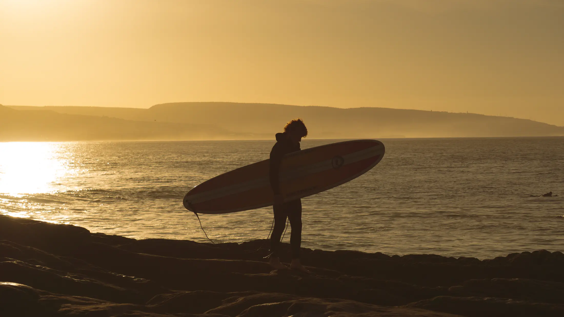 Surfer carrying a board beside the Atlantic at sunset